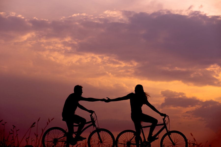 A couple riding bicycles toward the sunset, reaching for each other's hands